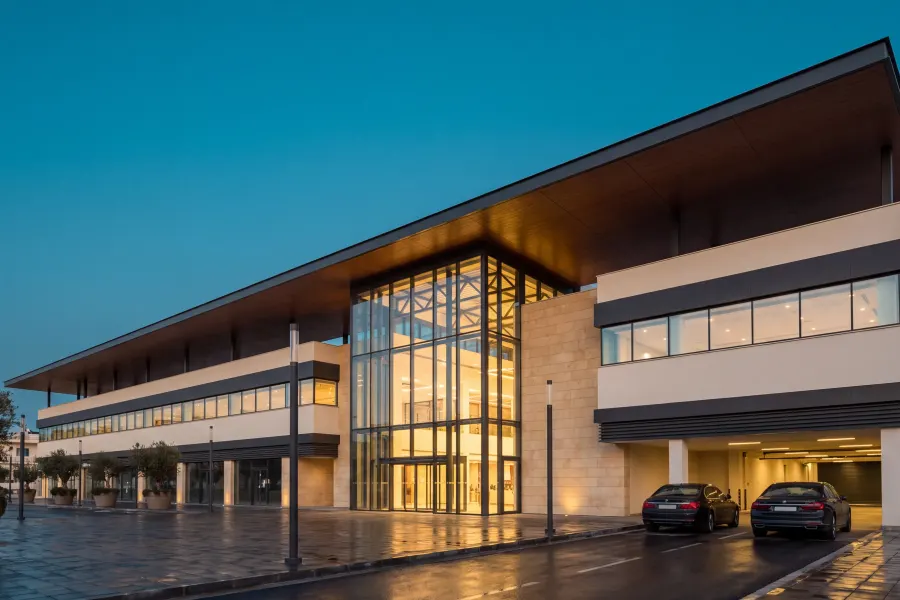 Two-storey retail and commercial building at dusk, a deep cantilevered canopy running the length of the facade over a full-height glazed atrium