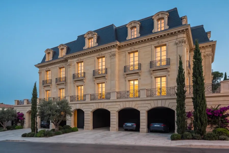 Three-storey honey-limestone mansion with a rusticated arcade of carports, wrought-iron balconies and a slate mansard with dormers