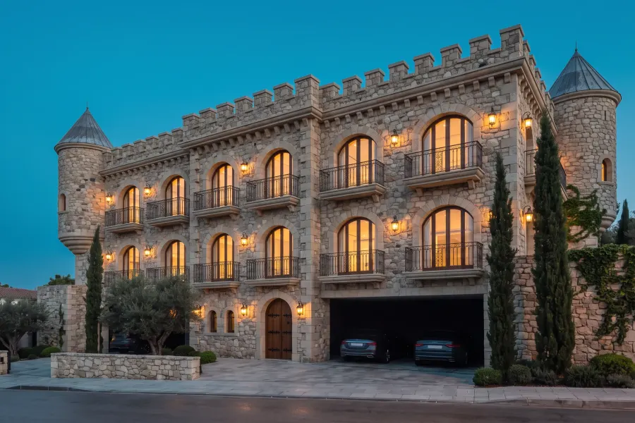 Three-storey stone building with a crenellated parapet, two conical turrets and arched windows, lantern-lit, with parking through the arch