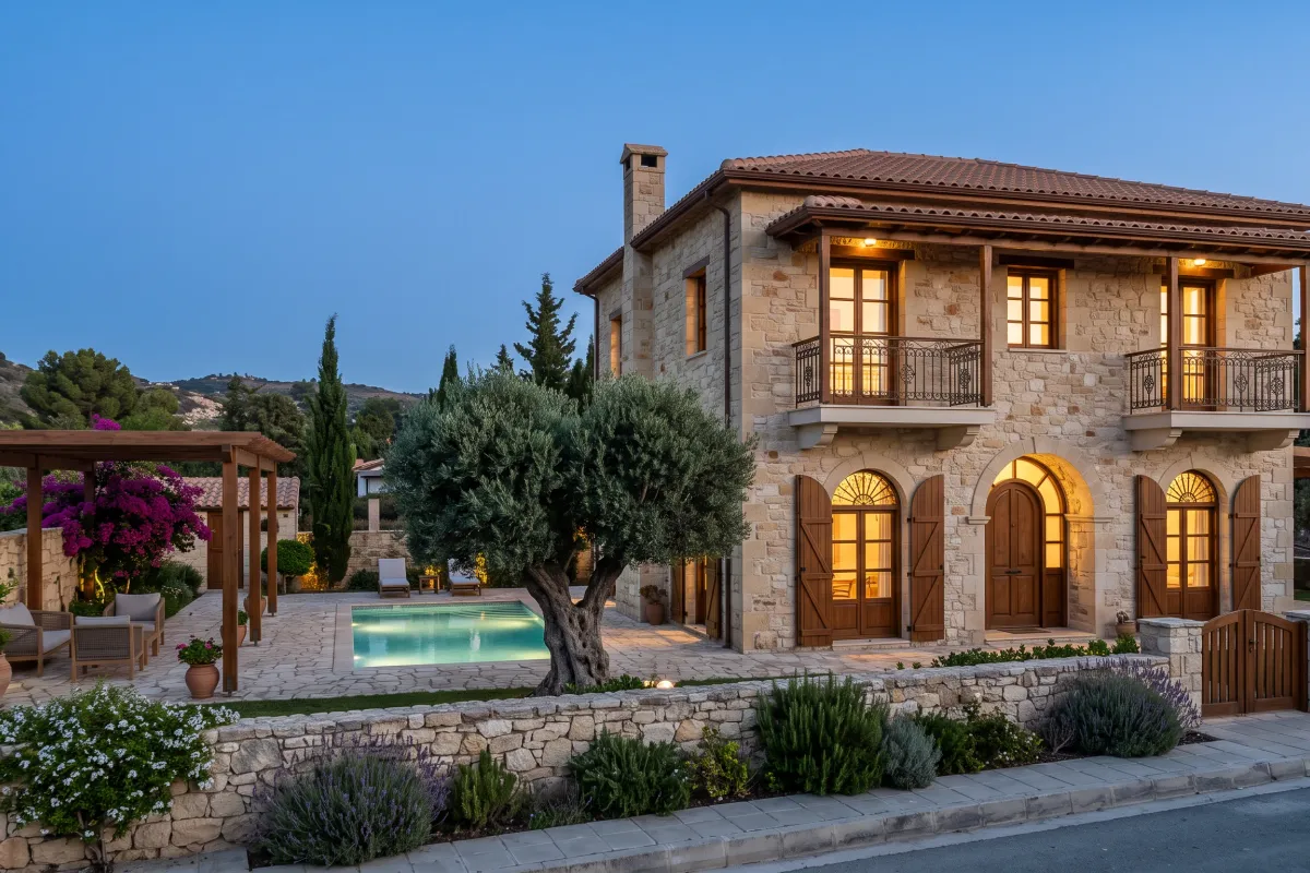 Two-storey villa in coursed Cypriot limestone with arched openings, timber shutters, a pergola-shaded courtyard and a pool